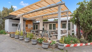 An outdoor seating area with wooden tables and chairs, surrounded by potted plants.