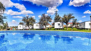 A swimming pool with a tiled edge, surrounded by mobile homes with red roofs, under a clear blue sky.