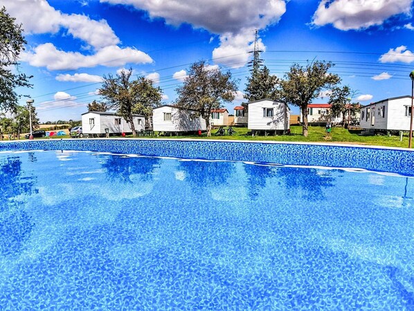 A swimming pool with a tiled edge, surrounded by mobile homes with red roofs, under a clear blue sky.
