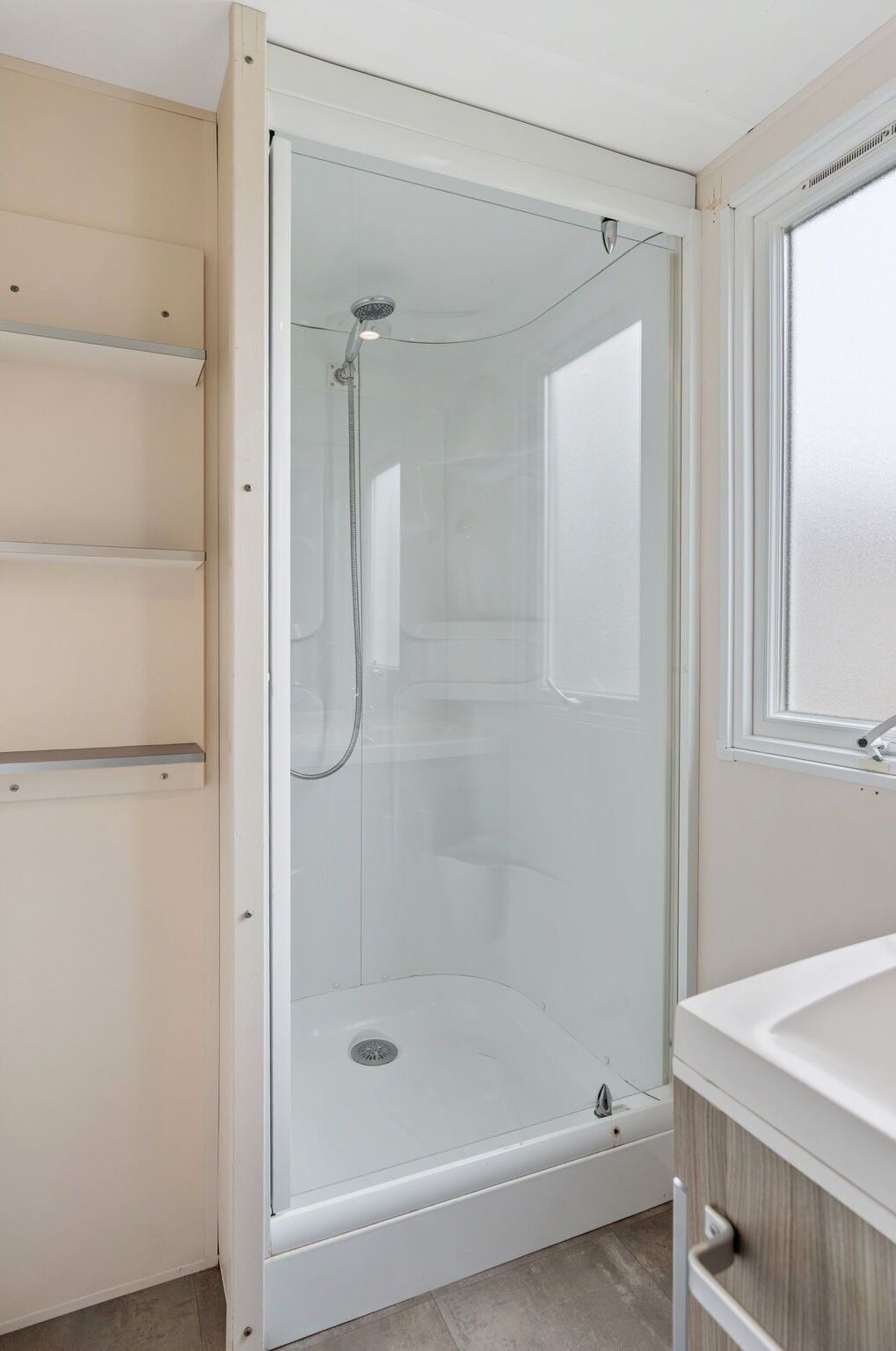 A modern bathroom with a glass-enclosed shower, a white sink, and a wooden vanity.