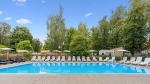 Ein Schwimmbecken mit Liegestühlen und Sonnenschirmen, umgeben von Bäumen und einem Gebäude.