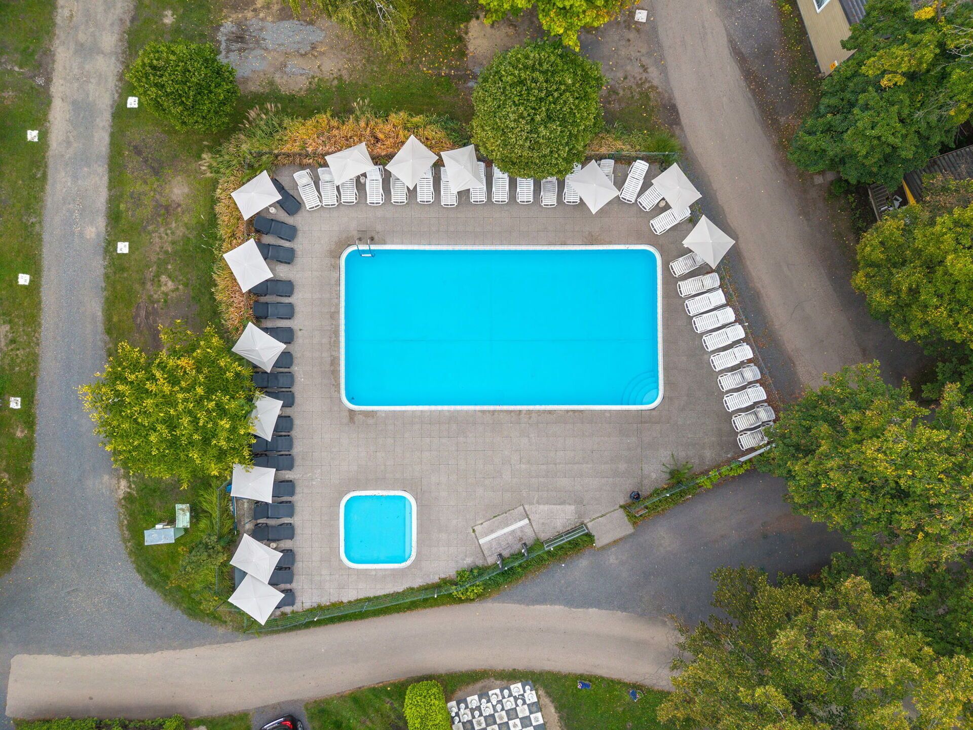 An aerial view of a swimming pool area with a rectangular pool, lounge chairs, and a smaller pool.