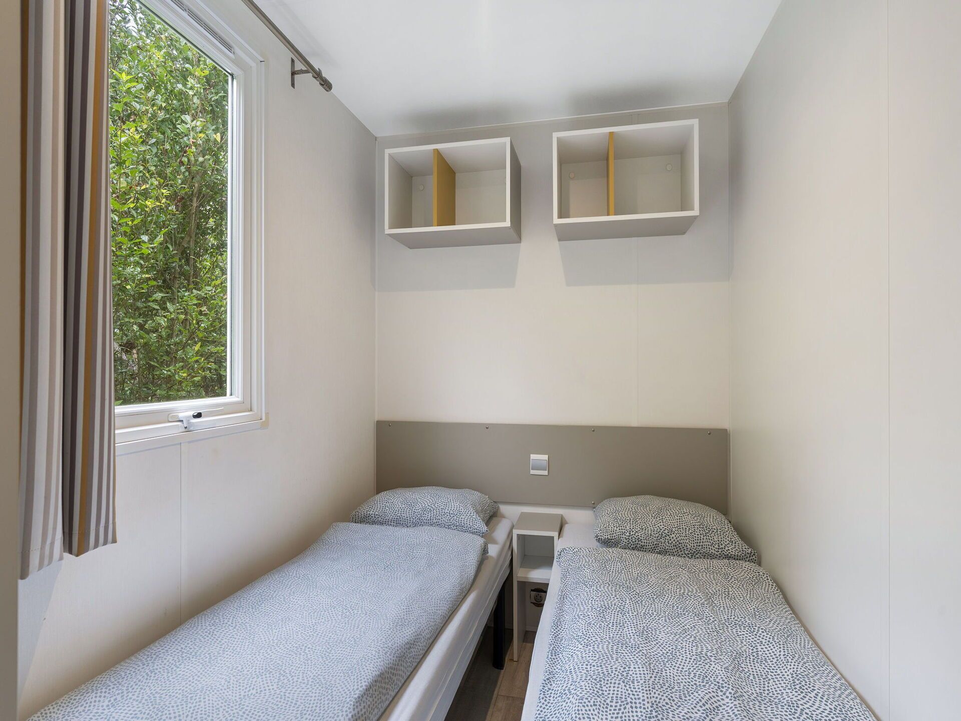 Een kleine, éénkameraccommodatie met twee éénpersoonsbedden, een raam en ingebouwde opbergkasten.