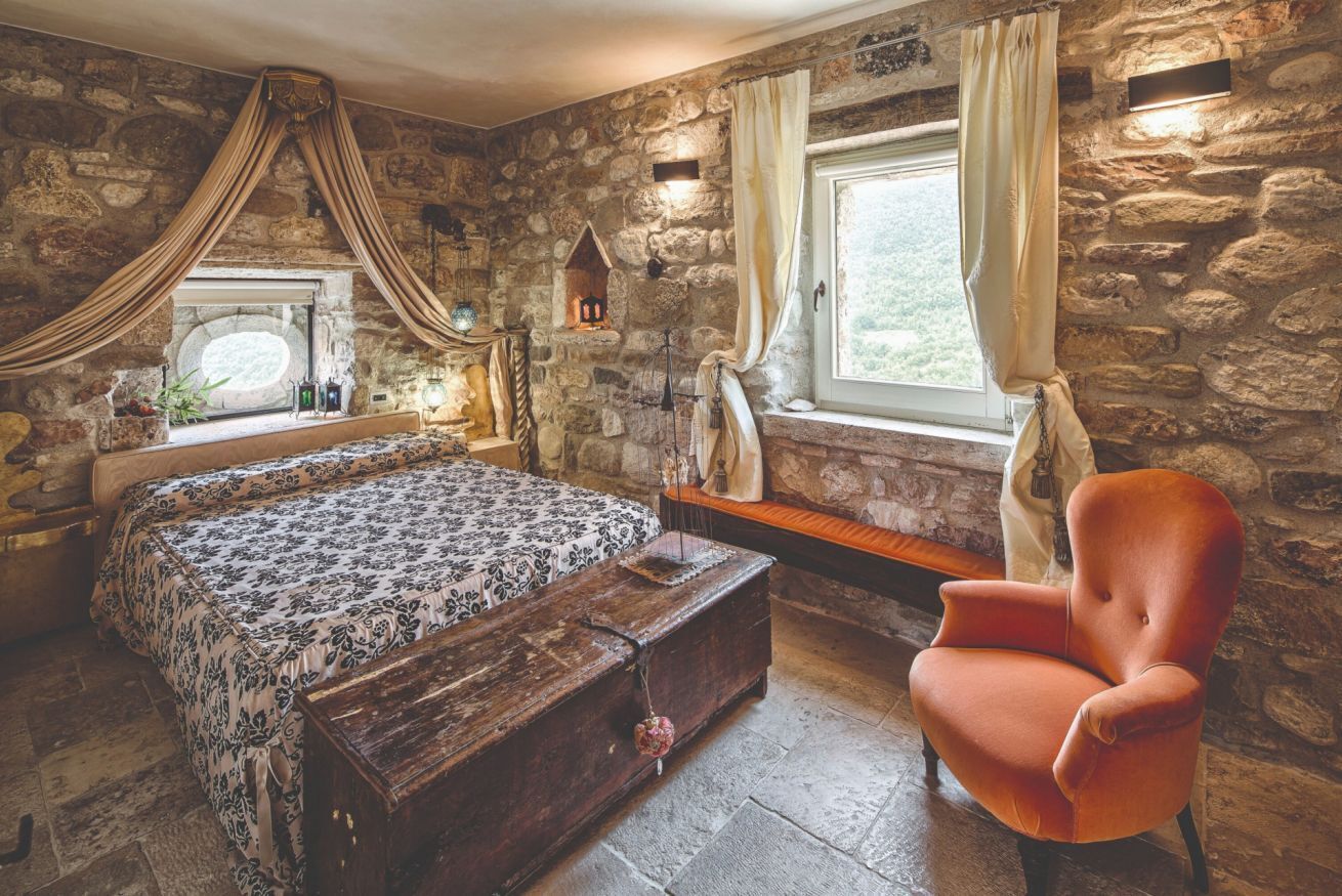 A stone-walled bedroom with a bed, bench, and chair.