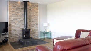 A modern living room with a stone wall, a fireplace, a leather sofa, and a glass coffee table. - Wonderful private villa for 6 guests with WIFI, TV, pets allowed and panoramic view (Tarskavaig)