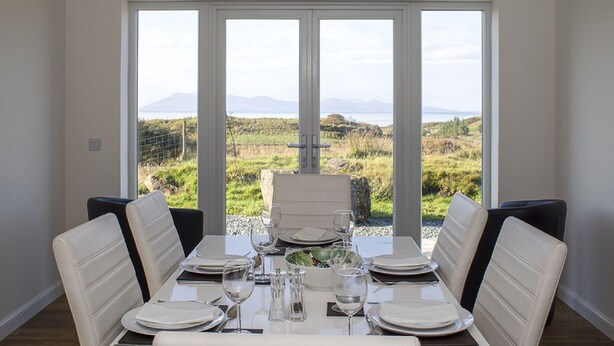 A dining area with a table set for four, large windows offering a view of a grassy landscape and mountains. - Wonderful private villa for 6 guests with WIFI, TV, pets allowed and panoramic view (Tarskavaig)