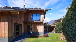 A modern two-story house with a wooden exterior, a large glass window, and a stone pathway leading to the entrance. - Wonderful private villa with A/C, hot tub, WIFI, private pool, TV, patio and pets allowed (Colico)
