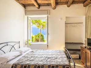 A bedroom with a bed, a window with a view of trees and mountains, a wooden ceiling, and a bathroom with a shower.