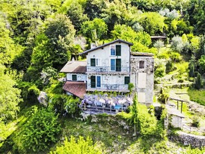 Un bâtiment à deux étages doté d’un balcon, entouré d’une végétation luxuriante et agrémenté d’un escalier en pierre.