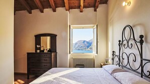 A bedroom with a bed, a dresser, a mirror, a radiator, and a window with a mountain view. - Beautiful apartment in villa for 6 guests with WIFI, TV, patio and pets allowed (Vendrogno)