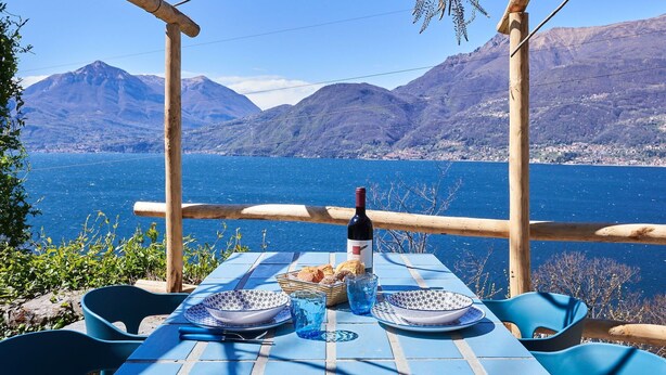 A table set outdoors with a bottle, bread, and plates, overlooking a lake with mountains in the background. - Lovely apartment in villa for 2 guests with WIFI, A/C, TV, terrace and pets allowed (Vendrogno)
