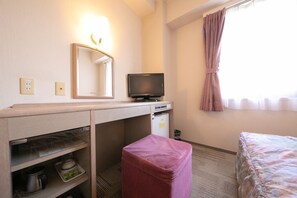 Una habitación de hotel con escritorio, televisión, refrigerador pequeño, un taburete rosa y una cama.