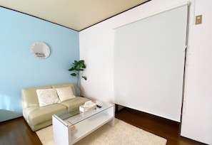 Una sala de estar moderna con un sofá beige, una mesa de centro de vidrio, un tapete blanco, un espejo redondo y una puerta grande de color blanco.