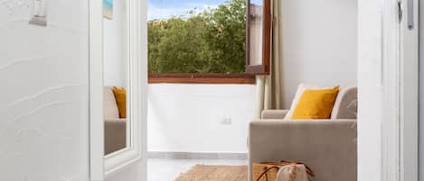A room with a large window, a sofa with a yellow pillow, and a woven basket on the floor.
