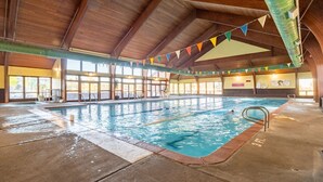 Una piscina interior con carriles delimitados, un trampolín y un techo de madera.
