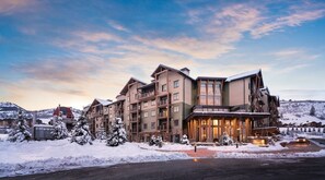 Un hotel de varios pisos con un telesilla visible al fondo, rodeado de árboles cubiertos de nieve.