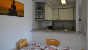 Een compacte keuken met een klein zithoekje, een schilderij aan de muur en één stoel.