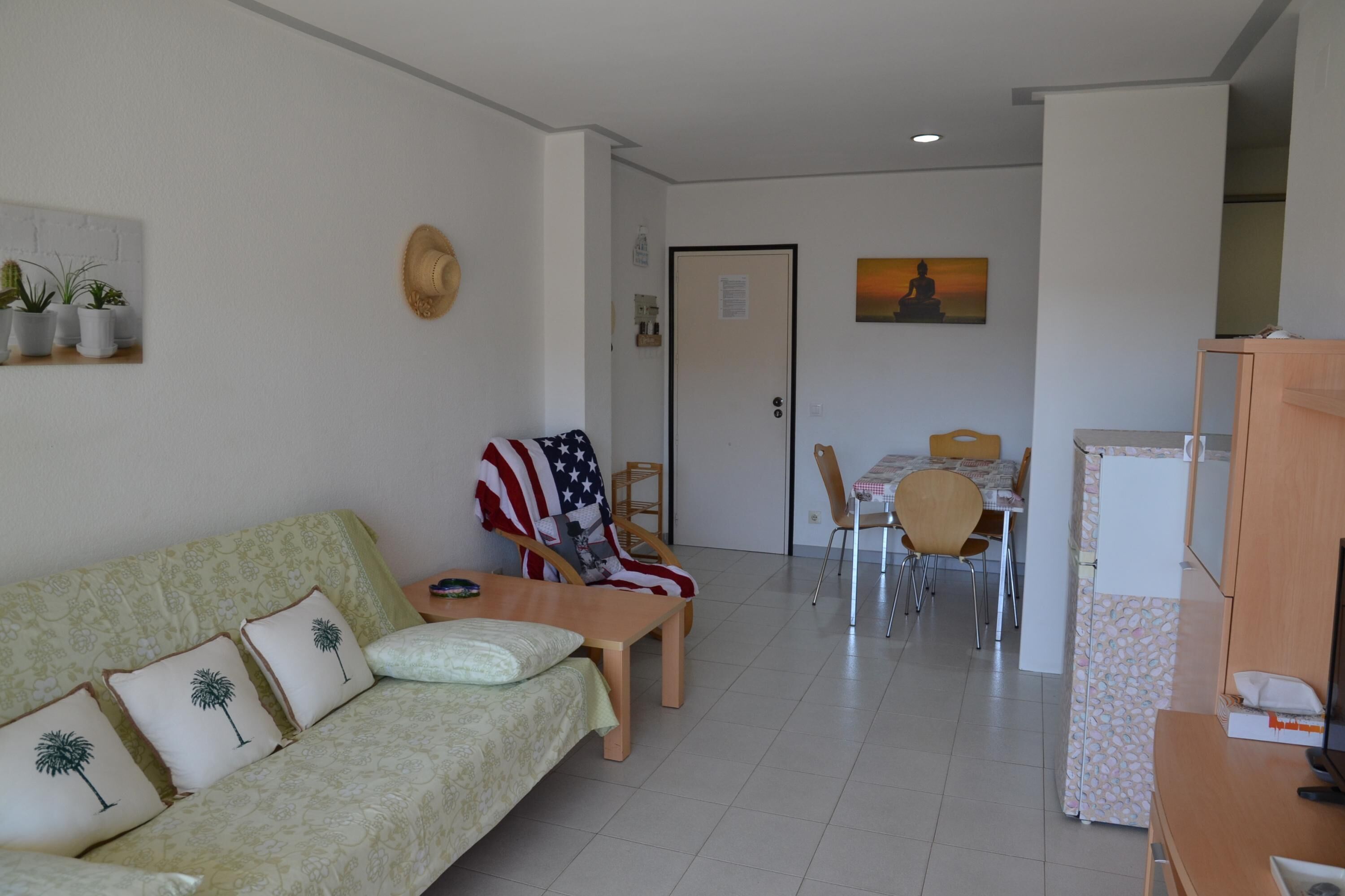 A living room with a sofa, a chair with an American flag, a dining table with chairs, and a refrigerator.