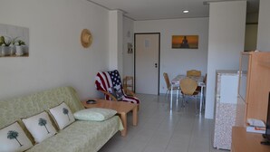Een woonkamer met een bank, een stoel met een Amerikaanse vlag, een eettafel met stoelen en een koelkast.
