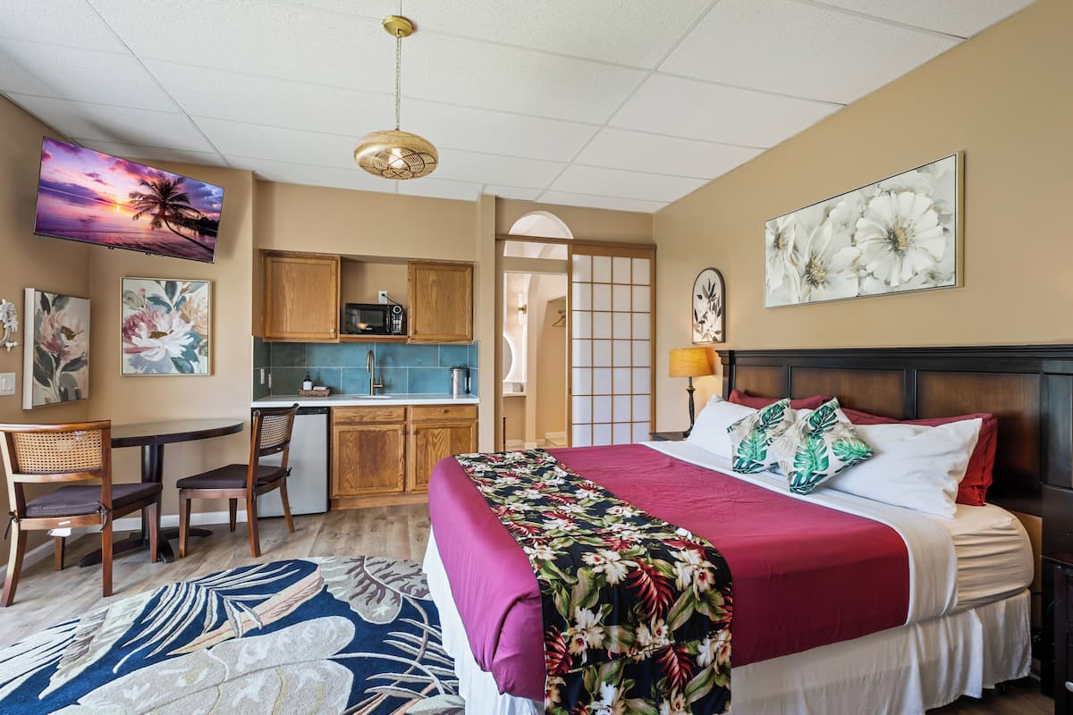 A hotel room with a bed, a desk, a kitchenette, and a TV on the wall.