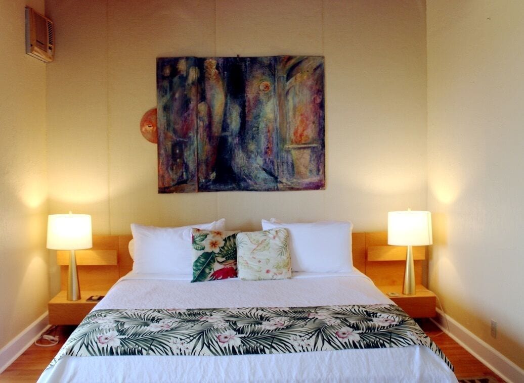 A hotel room with a large bed, two bedside lamps, and a colorful abstract painting on the wall.