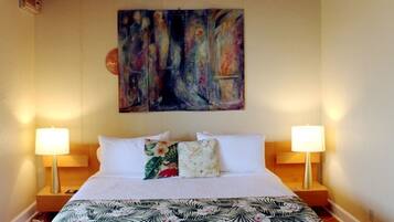 A hotel room with a large bed, two bedside lamps, and a colorful abstract painting on the wall.