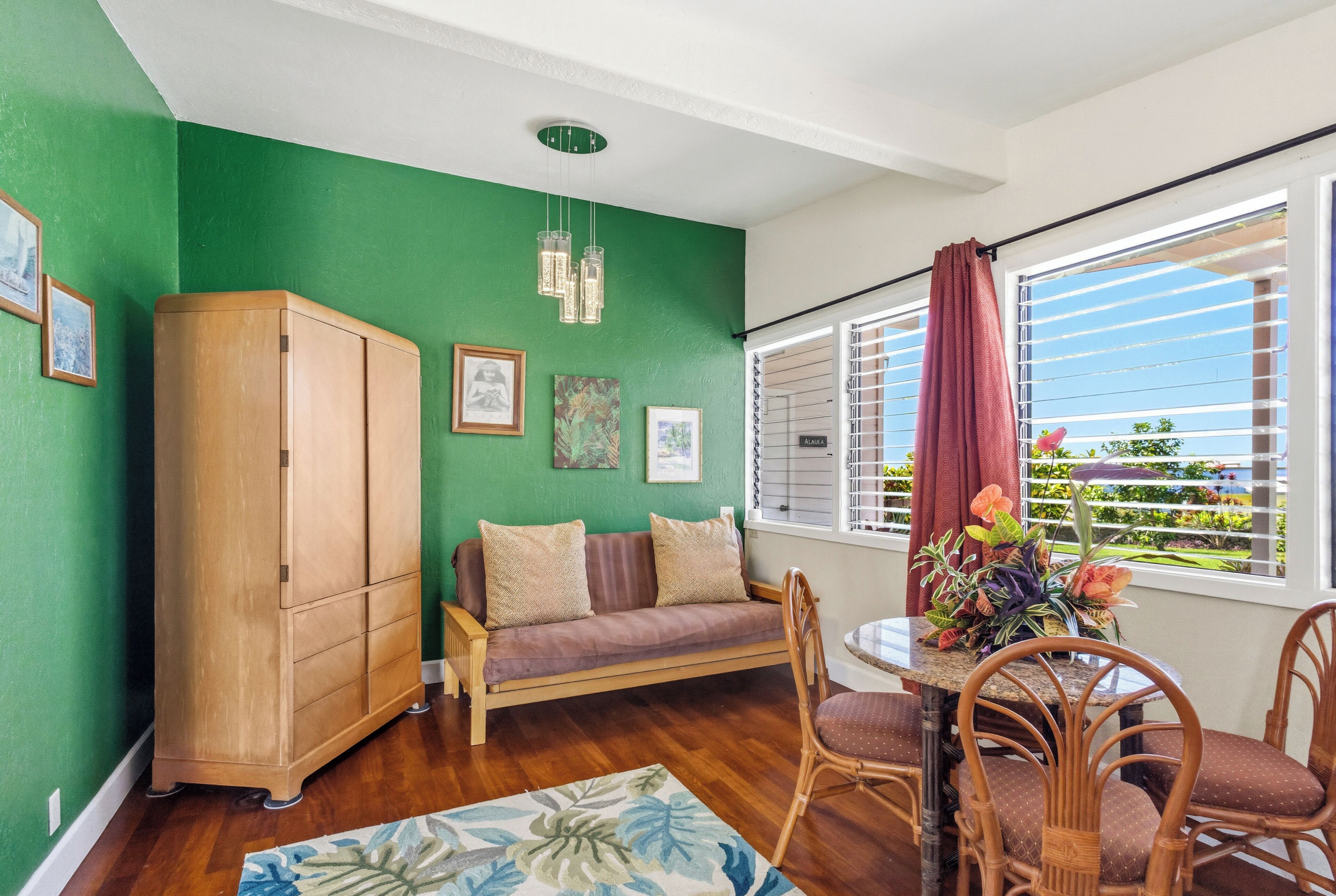 Una habitación con pared verde, muebles de madera, un sofá, una mesa de comedor con sillas y una ventana con persianas.