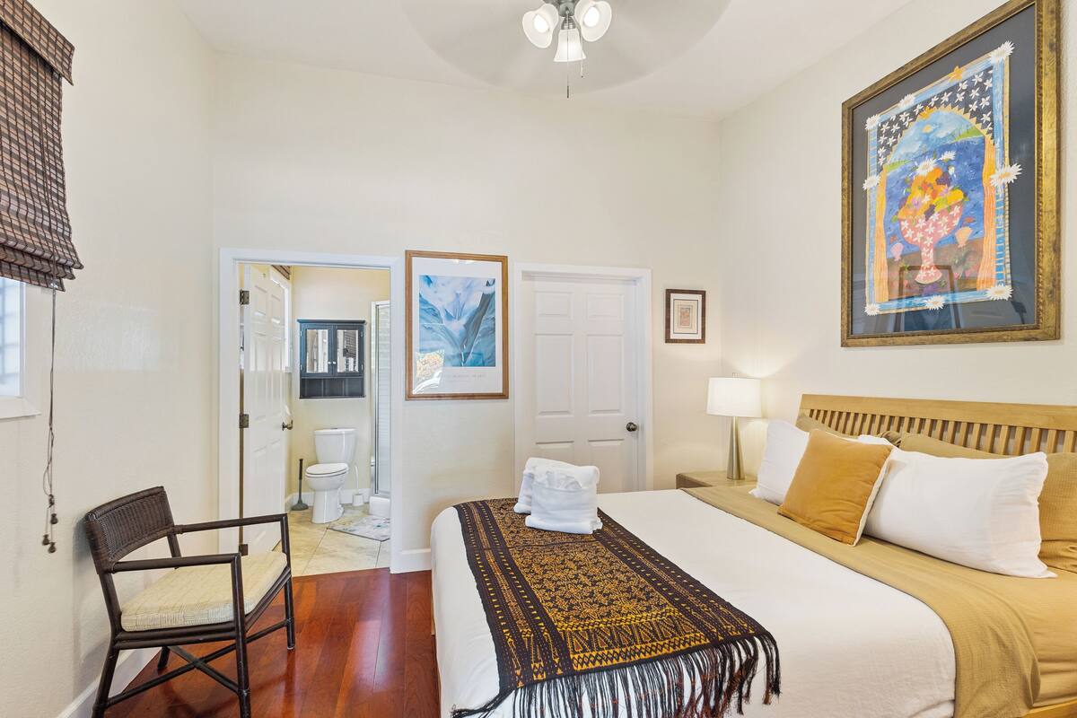 A hotel room with a bed, a chair, a door leading to a bathroom, and a painting on the wall.