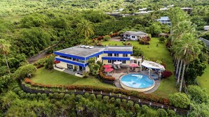 A modern two-story house with a swimming pool, surrounded by lush greenery and palm trees. - Luana Nai'a Inn (Captain Cook)