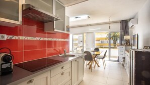 A modern kitchen with red tiles, a built-in stove, and a dining area with a table and chairs. - Apartment with swimming pool, close to the sea (Roses)