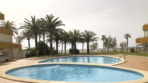 A swimming pool with a tiled deck, surrounded by palm trees and a view of the sea. - Apartment with swimming pool, close to the sea (Roses)