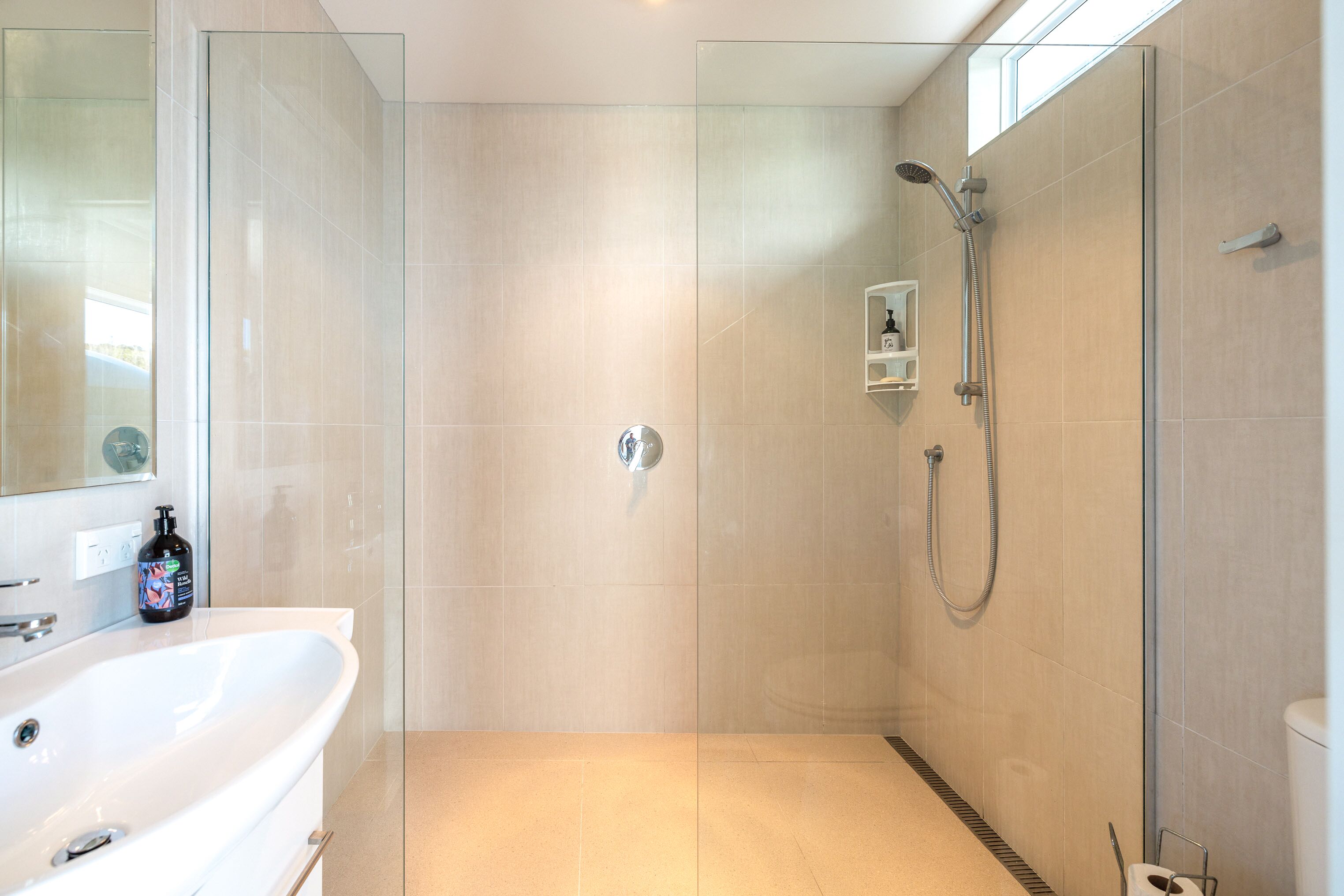 A modern bathroom with a glass-enclosed shower, a white bathtub, and a small shelf with toiletries.