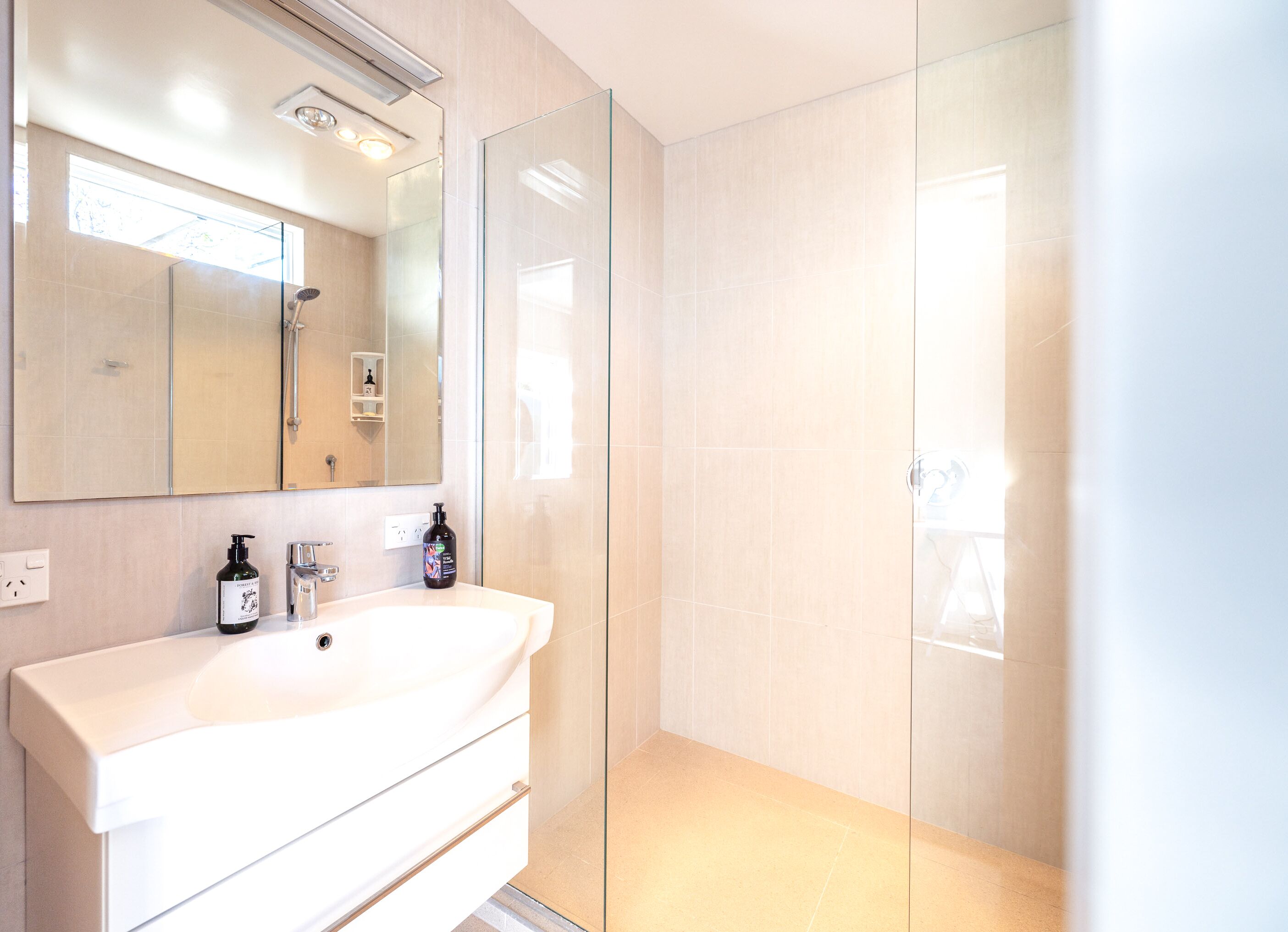 A modern bathroom with a white vanity, a glass shower enclosure, and a large mirror.