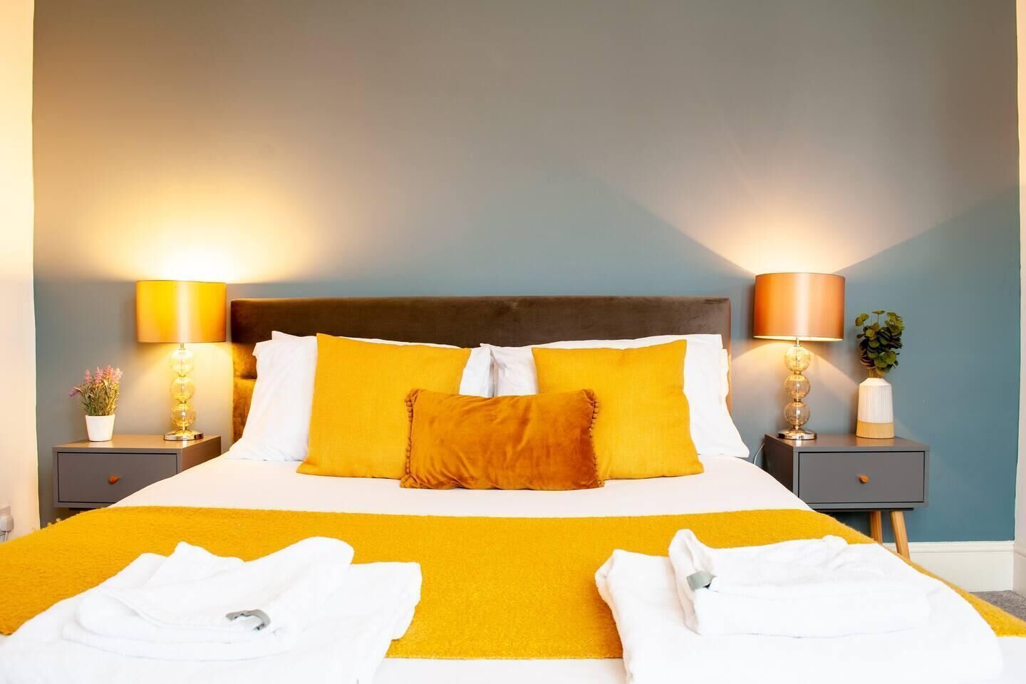 A hotel room with a large bed, two bedside tables with lamps, and a nightstand with a plant.