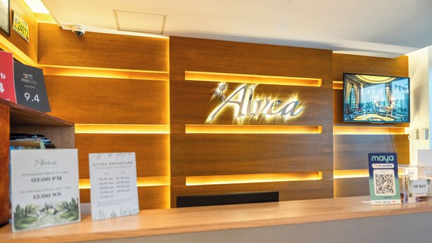 A reception desk with a wooden panel design, a large screen displaying a scenic view, and a sign with the name 'Alvea'. - Alvea Hotel (Puerto Princesa)