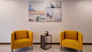 A room with two yellow armchairs, a small table with a vase, and a wall with multiple framed pictures. - Alvea Hotel (Puerto Princesa)