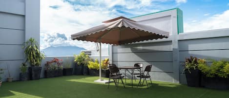 Un patio con césped artificial, una mesa con sillas y un gran paraguas.