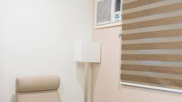 Une pièce avec une chaise en bois, une petite table, un radiateur et une fenêtre avec des stores.
