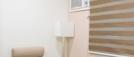Una habitación con una silla de madera, una mesita pequeña, un calentador portátil y una ventana con persianas.