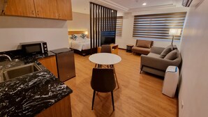 A compact hotel room with a kitchenette, a dining area, a sofa, and a bed with a TV. - Alvea Hotel (Puerto Princesa)