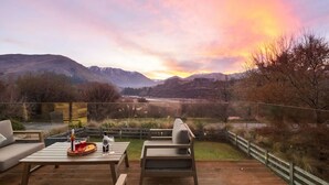 Une terrasse dotée de mobilier d’extérieur, offrant une vue sur un paysage montagneux au coucher du soleil.