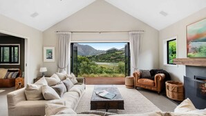 Un salon spacieux doté d’une grande fenêtre offrant une vue panoramique sur les montagnes, d’un canapé confortable, d’une cheminée et d’un coin salon accueillant.