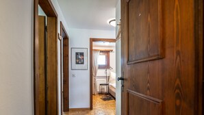 Un corridoio con pavimento in legno e porte che conduce a una camera da letto con un letto e una finestra.