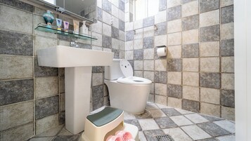 A bathroom with a toilet, sink, and a shelf with toiletries.