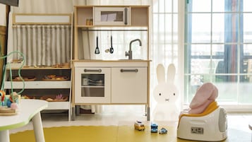 Un espace de jeux pour enfants avec un plan de travail de cuisine, des placards de rangement et une grande fenêtre.