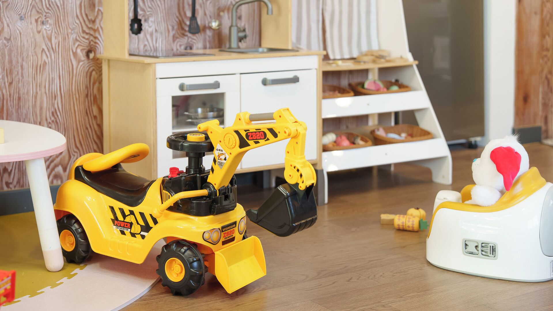 Una excavadora de juguete y un bulldozer de juguete en una habitación con suelo de madera, un armario blanco y una pequeña mesa redonda.