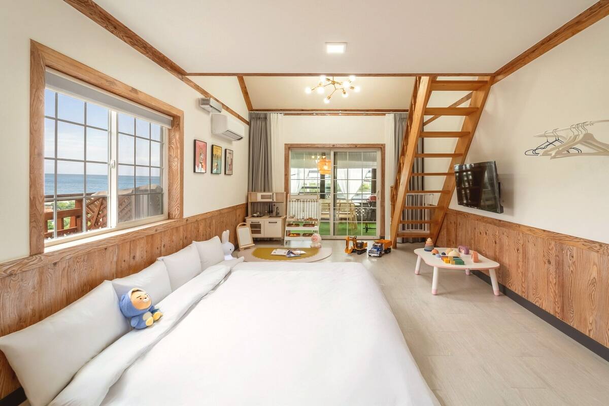 Une chambre d’hôtel avec un grand lit, un banc en bois, une petite table avec des jouets, une télévision et une vue sur l’extérieur.