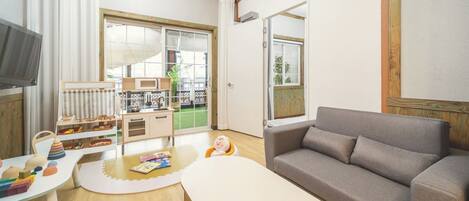 A modern living room with a grey sofa, a small white table, and a play area with toys and a bookshelf.