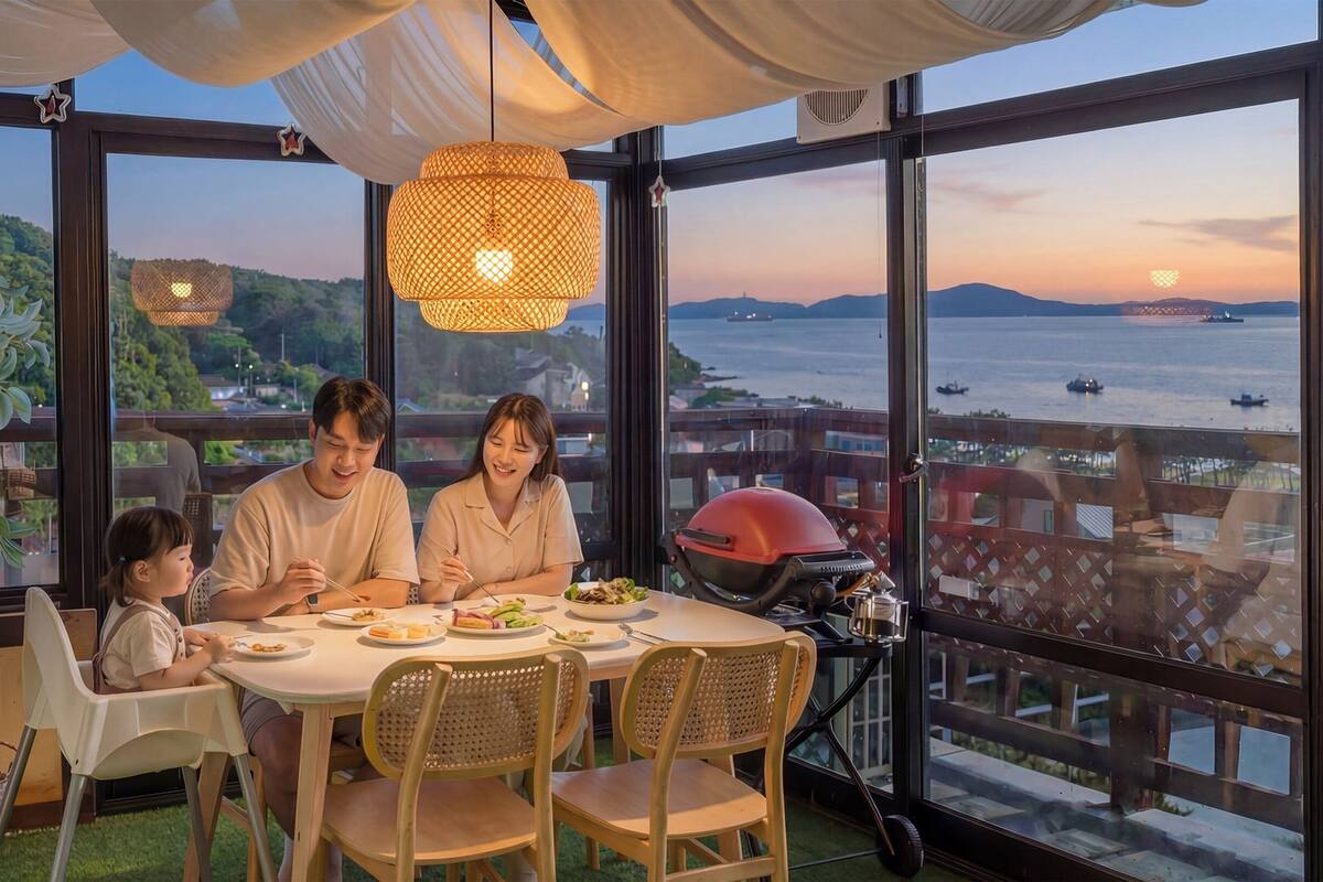 Un espace repas offrant une vue sur la mer et les montagnes, avec des chaises en osier, une table dressée avec des plats et un barbecue.