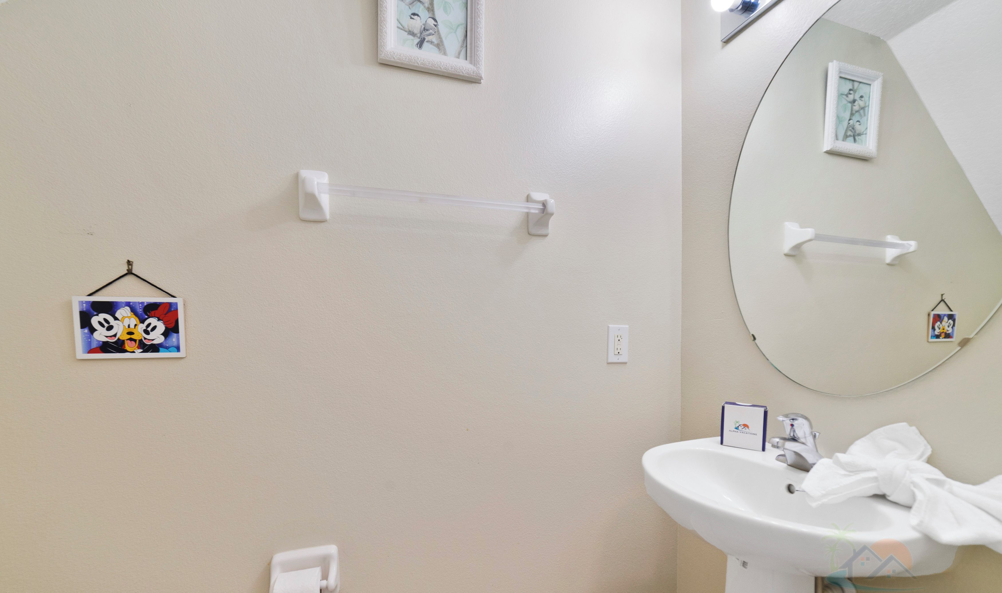 A bathroom with a white sink, a mirror, and two towel racks. There are two framed pictures on the wall.